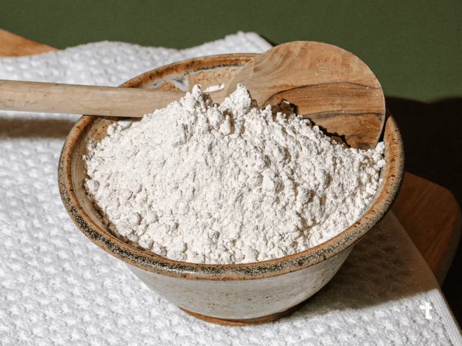 A bowl of fonio flower is displayed on a cutting board with a wooden spoon