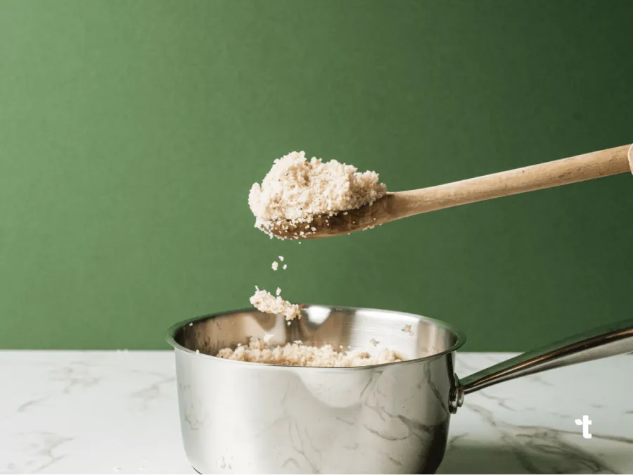 A wooden spoon shown scooping cooked, pearled fonio from a sauce pan.