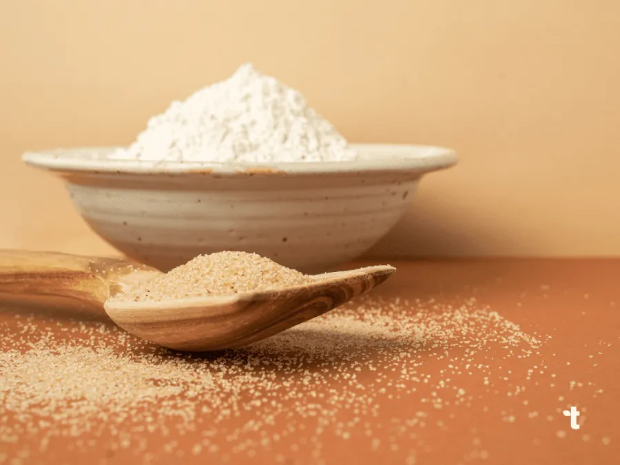 Pearled fonio and fonio flour are displayed on a wooden spoon and in a ceramic bowl