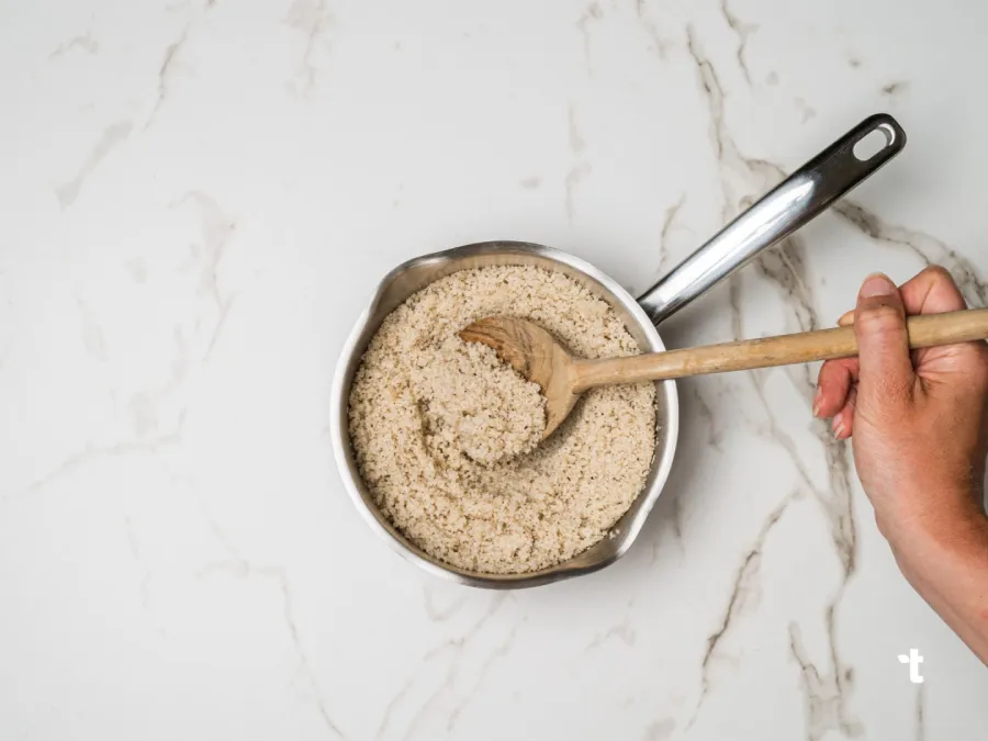 Cooked fonio being stirred in a pot with a wooden spoon