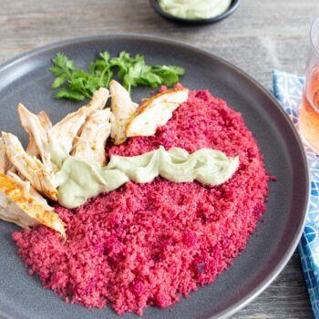 A plate of feet red fonio with chicken and avocado crema is displayed with a glass of iced tea.