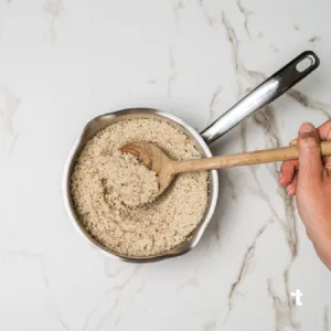 Cooked fonio being stirred in a pot with a wooden spoon