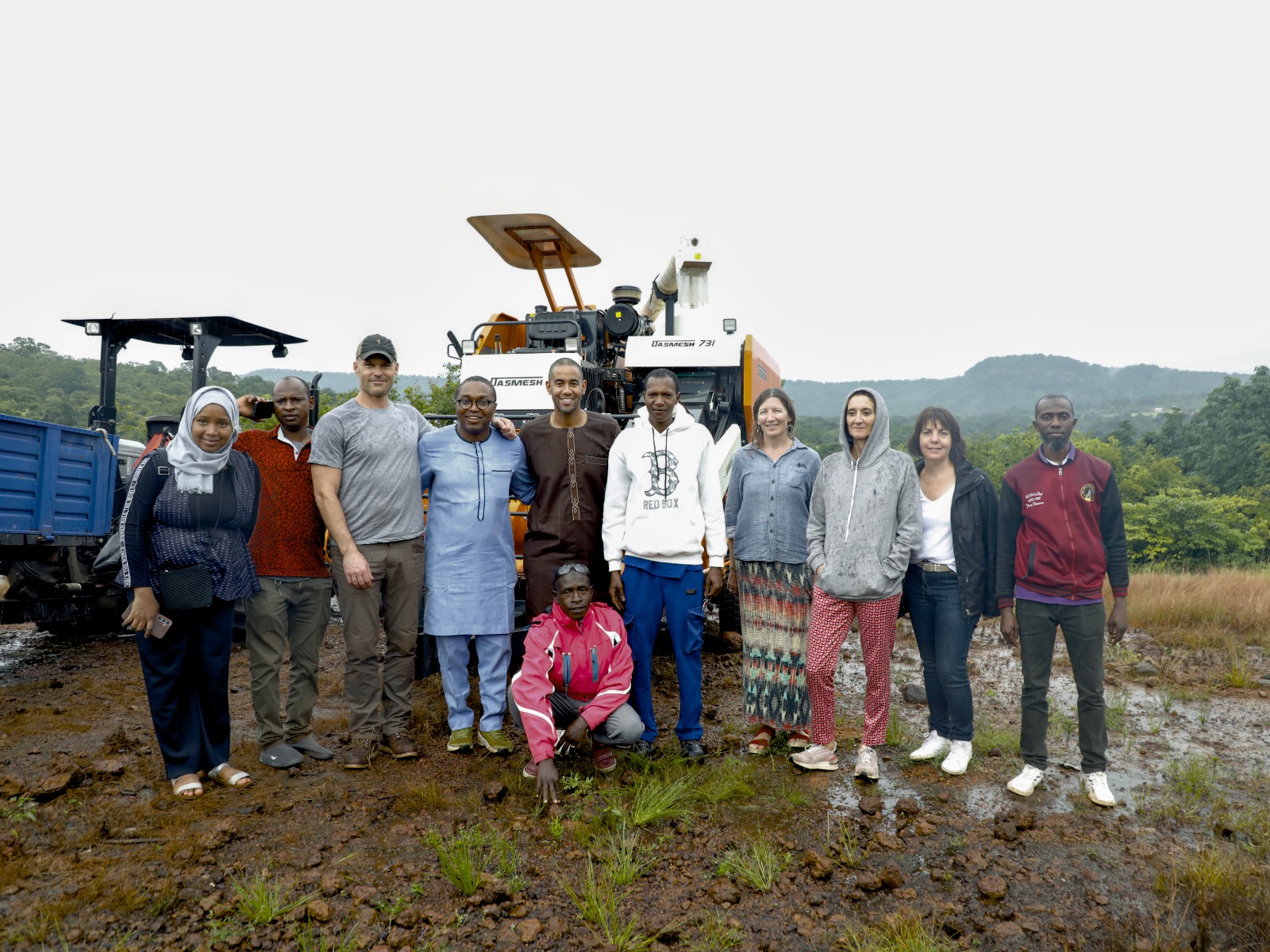 A group of fonio farmers and their guests stand in front of a front end loader in Guinea.