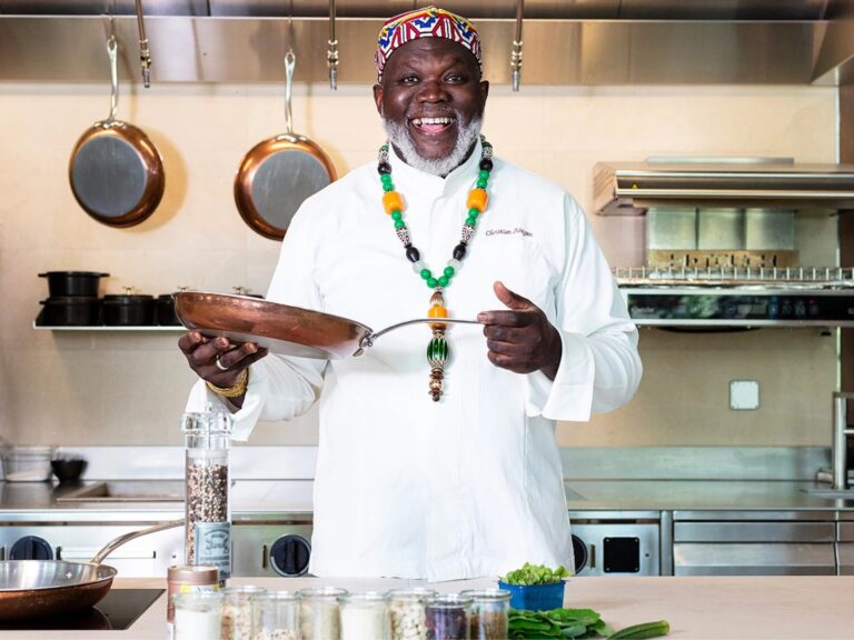 Chef Abegan holds a frying pan as he poses for a photo in a kitchen