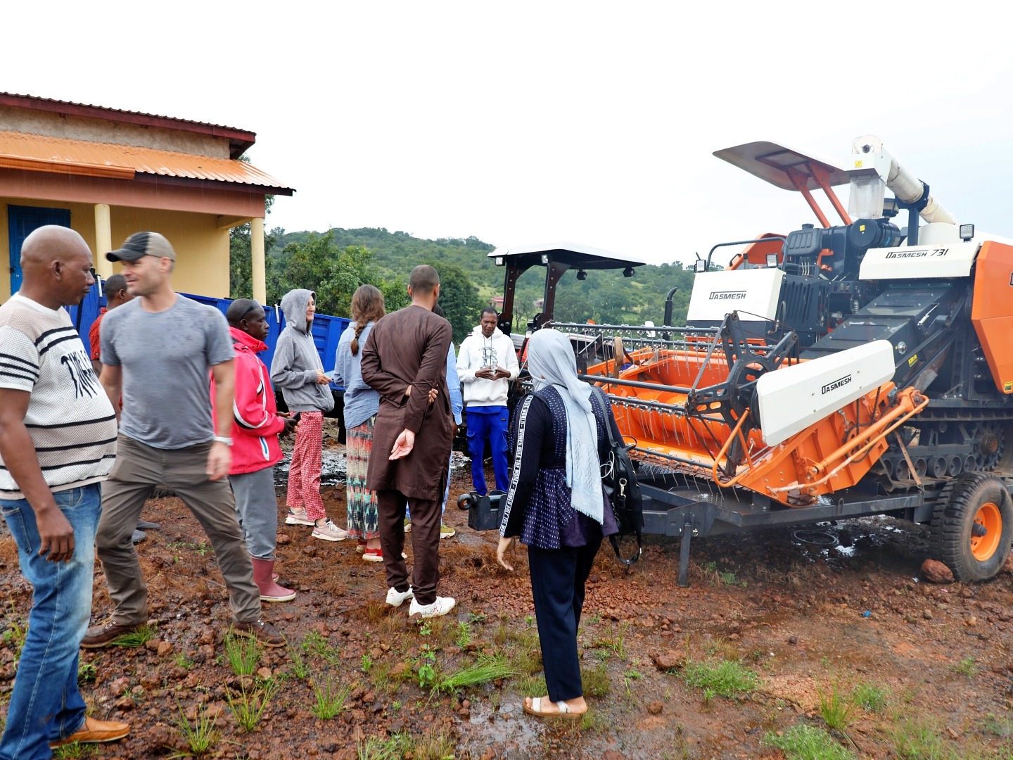 A group of men and women gather to talk in front of a large farming tractor on a muddy farm