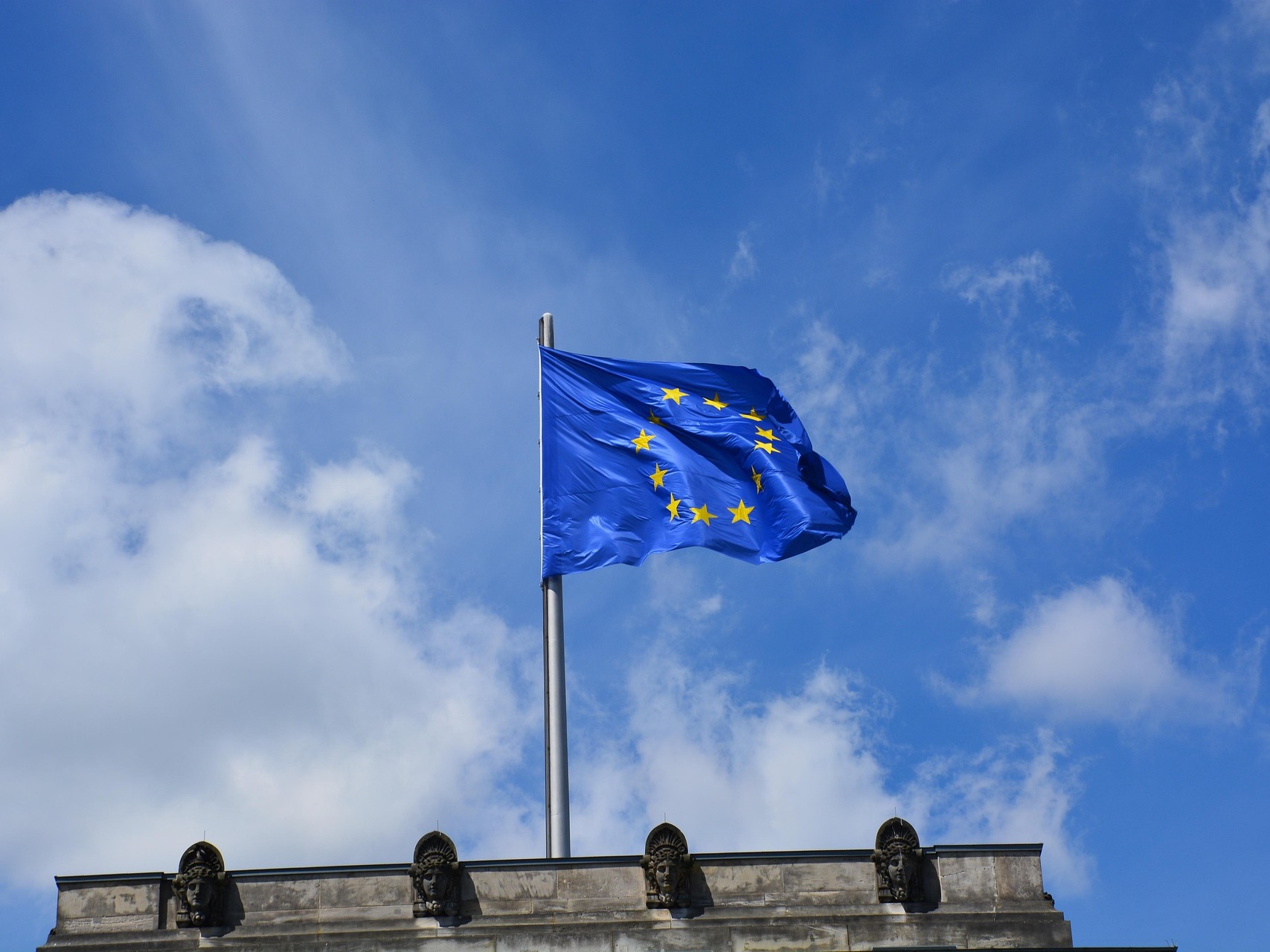 The European Union flag waves set against a slightly cloudy, blue sky