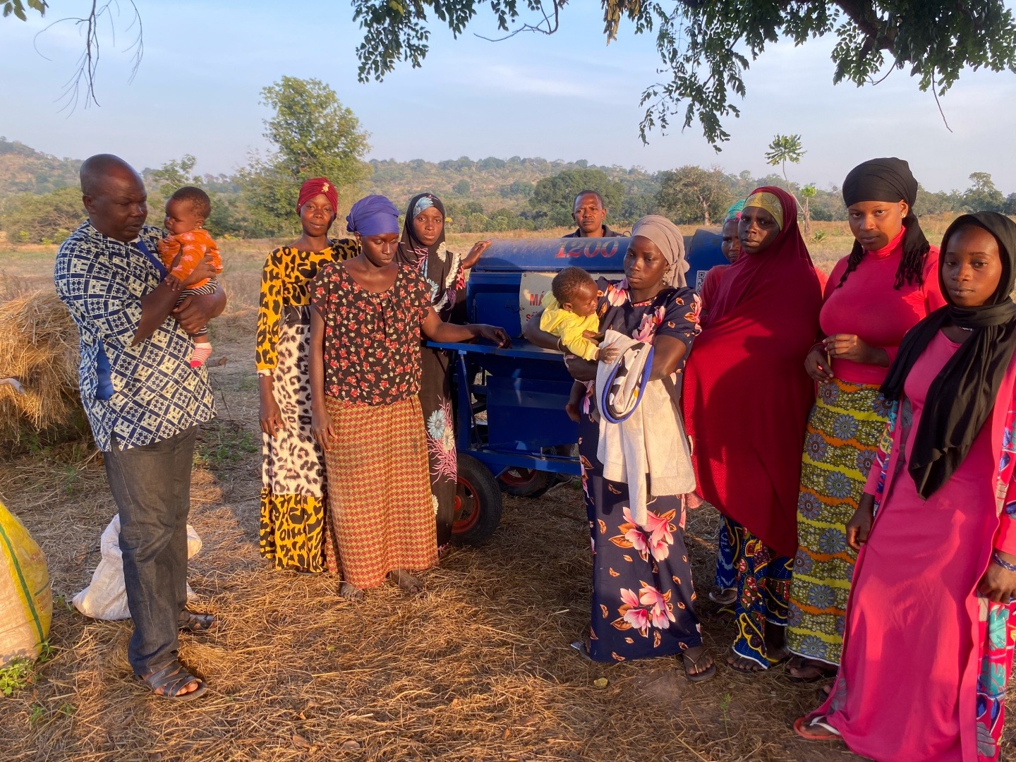 A group of men, women and children in rural Guinea pose for a photo next to a fonio thresher